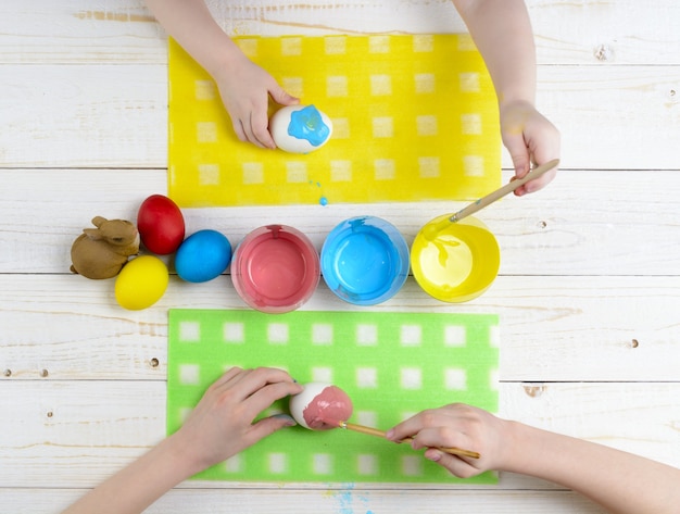 Kinder malen Eier für Ostern auf dem Holztisch