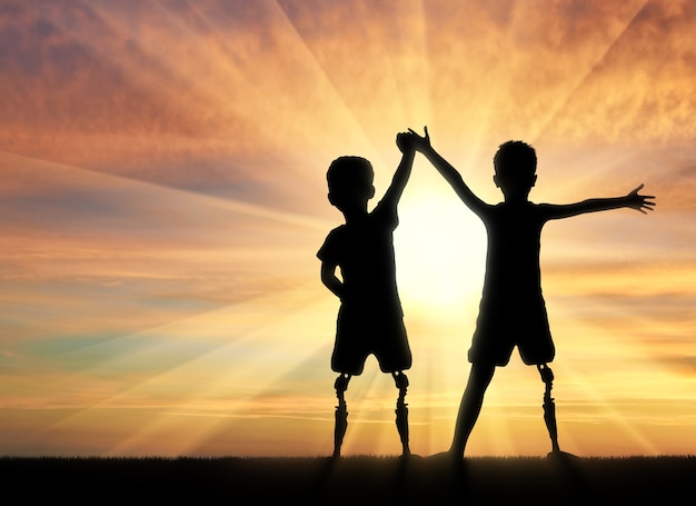 Kinder mit Behinderungen. Zwei Jungen einer behinderten Person mit einer Beinprothese stehend, Händchen haltend auf Sonnenuntergangshintergrund
