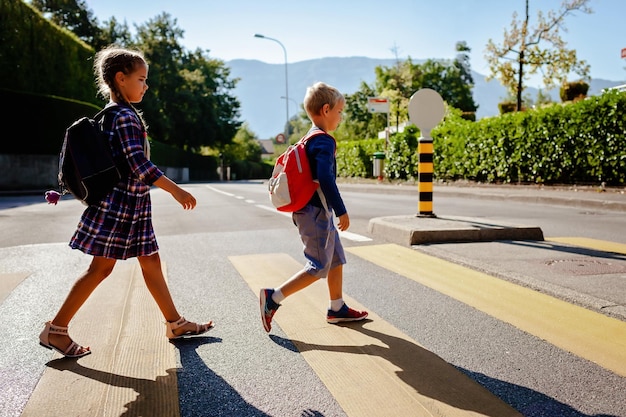 Kinder mit Rucksäcken überqueren die Straße am Fußgängerübergang auf dem Weg zur Schule