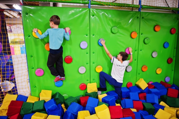 Kinder mit zwei Brüdern klettern auf einer grünen Wand im Attraktionsspielplatz.