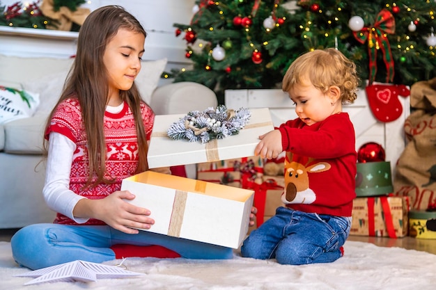 Kinder öffnen Weihnachtsgeschenke unter dem Baum Selektiver Fokus