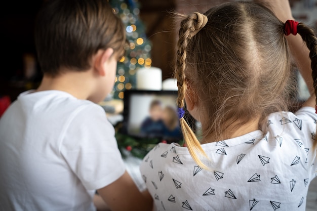 Kinder rufen sich per video an, um in der winterpause in kontakt zu bleiben. kleiner junge mit weihnachtsmütze sitzt vor dem computerbildschirm und chattet online mit einer gruppe seiner verschiedenen freunde am heiligabend zu hause