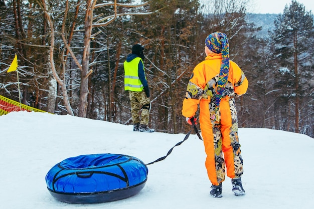 Kinder rutschen mit einer Schnee-Röhre über einen verschneiten Hügel hinunter.