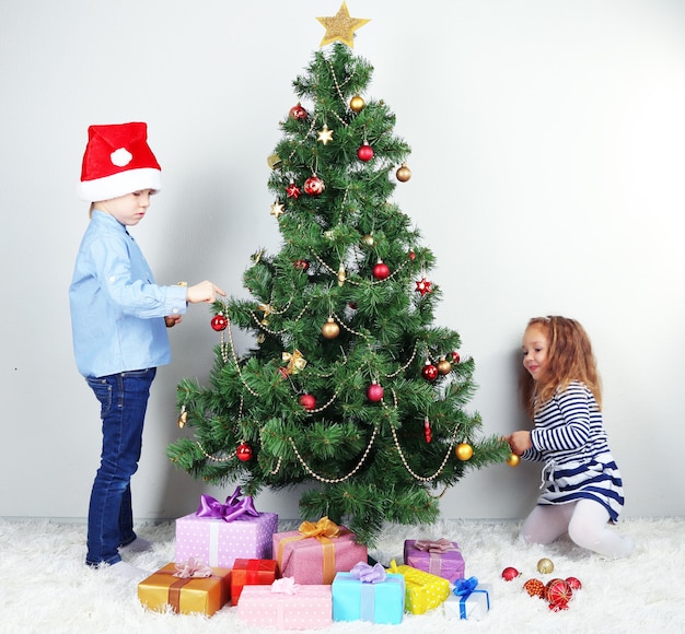 Kinder schmücken Weihnachtsbaum mit Kugeln im Zimmer