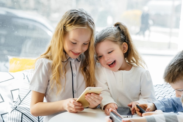 Kinder sitzen an einem Tisch in einem Café und spielen zusammen Handys. Moderne Unterhaltung.