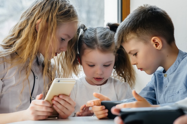 Kinder sitzen an einem Tisch in einem Café und spielen zusammen Handys. Moderne Unterhaltung.