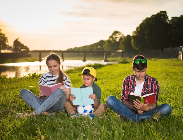 Kinder sitzen auf dem Gras mit Büchern im Park bei Sonnenuntergang. Sonniger Sommertag