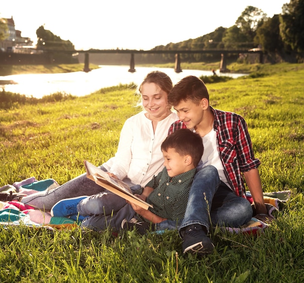 Kinder sitzen auf dem Gras und lesen Buch im Park. Sonniger Sommertag