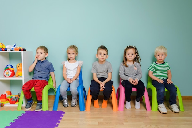 Kinder sitzen auf den bunten Stühlen im Kindergarten Die Kinder warten auf den Unterricht