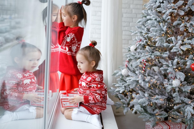 Kinder sitzen auf der Fensterbank beim Weihnachtsbaum und schauen durch das Fenster auf die Straße