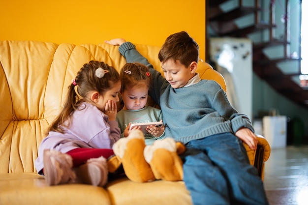 Kinder sitzen auf einem Ledersofa im Wohnzimmer und schauen sich Zeichentrickfilme am Telefon an