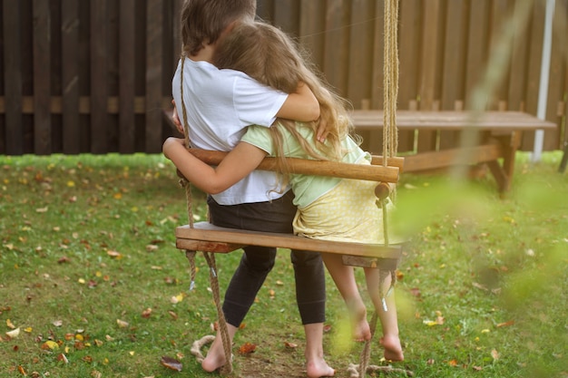 Kinder sitzen auf einer Schaukel im Garten älterer Bruder umarmt kleine Schwester