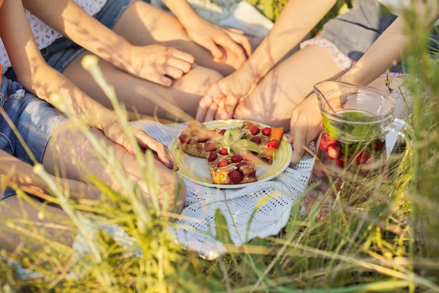 Foto kinder sitzen auf gras und essen hausgemachten kuchen mit beeren, trinken minze erdbeergetränk