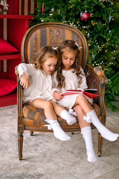 Kinder sitzen auf Stühlen am Weihnachtsbaum und lesen Märchen