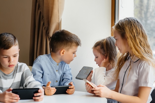 Kinder sitzen im Café am Tisch und spielen zusammen Handys.