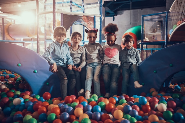 Kinder sitzen im Pool voller bunter Bälle