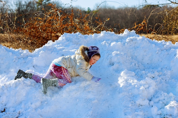 Kinder spielen außerhalb der Wintersaison Glückliches Kind spielt im Schnee in der Nähe eines Waldes