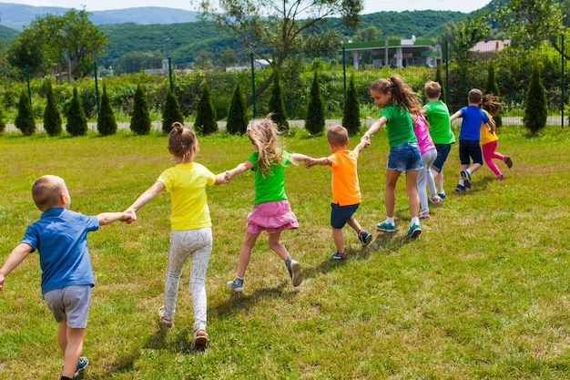 Kinder spielen Händchen haltend auf dem grünen Rasen. Kinder laufen hintereinander und genießen gemeinsam. Sommerspiele im Freien