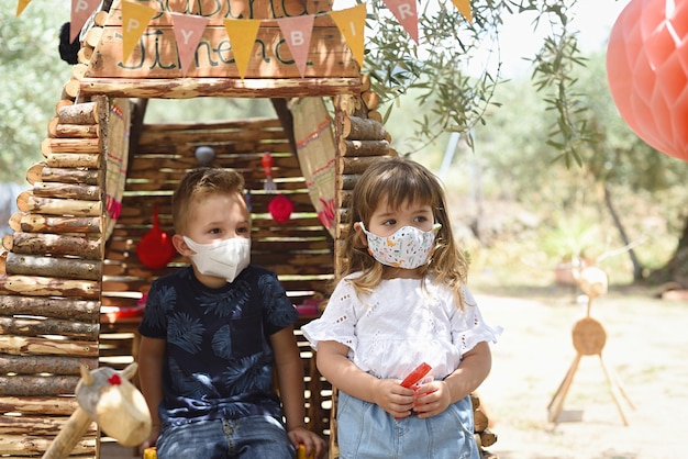 Kinder spielen im Freien in einem Holzhaus mit einer Maske