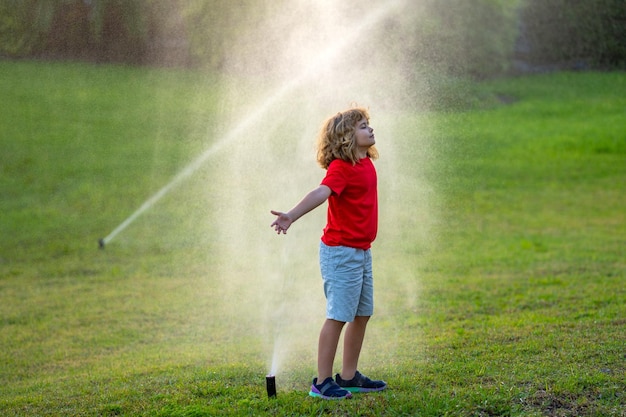 Foto kinder spielen im sommergarten, bewässern das automatische sprinklerbewässerungssystem in einem grünen park