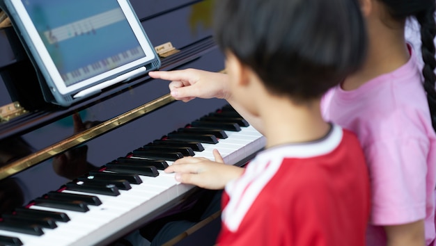 Kinder spielen Klavier zusammen mit Tablet-Lernen zu Hause online in der Krise 19