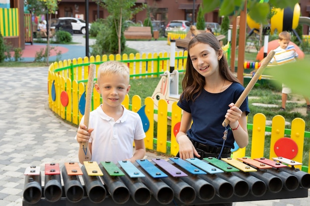 Kinder spielen mit einem Hammer auf einem Straßenmusikinstrument ein mehrfarbiges Xylophon im Park