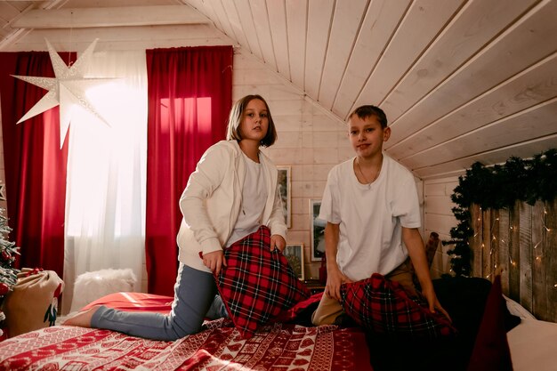 Kinder spielen mit Kissen auf dem Bett im weihnachtlich dekorierten Schlafzimmer, Kissenschlachten, das Konzept der Neujahrsferien