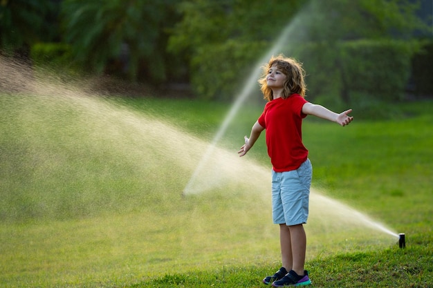 Kinder spielen mit Wasserschlauchsprinkler, bewässern Gras im Garten, Sommergarten, Outdoor-Spaß für Kinder