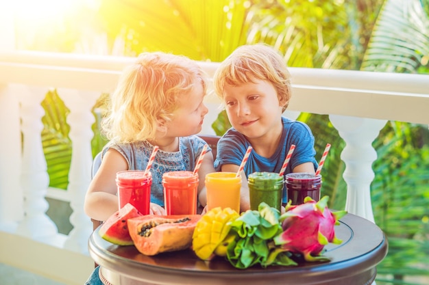 Kinder trinken bunte gesunde Smoothies.. Wassermelone, Papaya, Mango, Spinat und Drachenfrucht. Smoothies, Säfte, Getränke, Getränkevielfalt mit frischen Früchten auf einem Holztisch