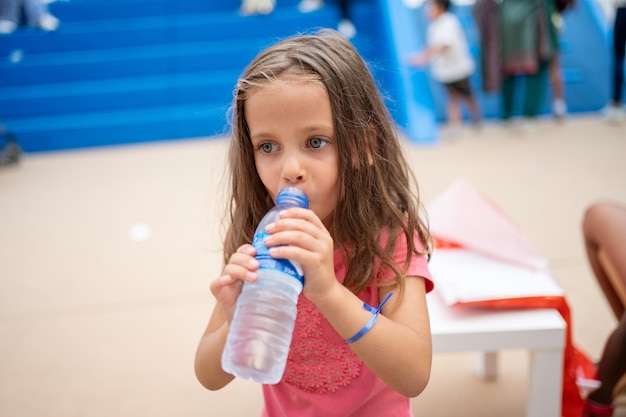 Kinder trinken Wasser aus Plastikflaschen im Freien