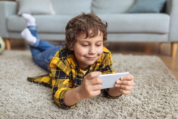 Kinder und Internetsucht Nahaufnahme eines kleinen Jungen, der sich Videoinhalte auf dem Smartphone ansieht, das auf dem freien Platz auf dem Boden liegt