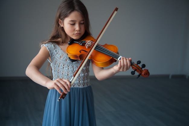 Kinder und Musikinstrumente Kleines brünettes Mädchen in einem schönen Kleid, das drinnen Geige spielt