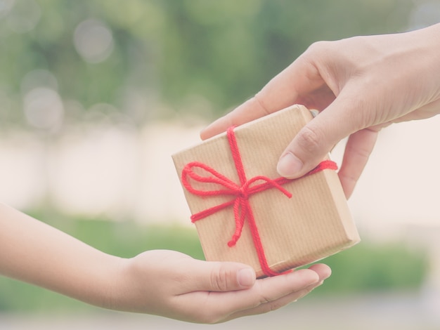 Kinder- und Mutterhände mit Geschenkbox über grünem Hintergrund