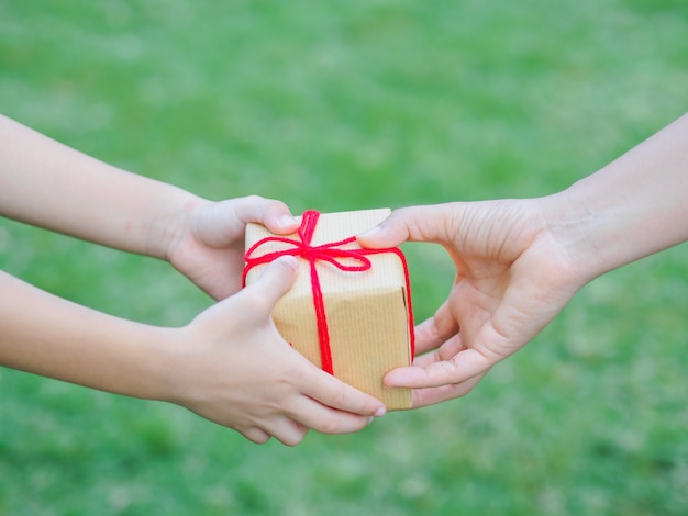 Kinder- und Mutterhände mit Geschenkbox über grünem Hintergrund