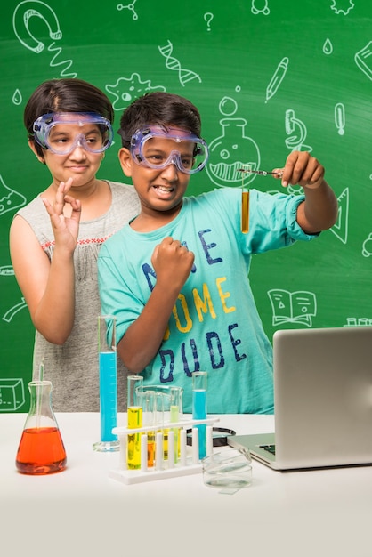 Kinder- und Wissenschaftskonzept - süßer indischer kleiner Schüler oder Wissenschaftler, der Wissenschaft studiert oder mit Mikroskop und Chemikalien experimentiert, mit Diagrammen, die über grüne Tafel gezeichnet sind