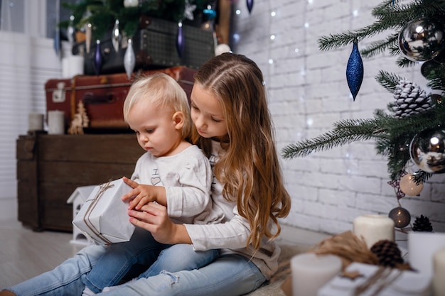 Kinder unter Weihnachtsbaum mit Geschenkboxen. Dekorationen für das neue Jahr. rustikaler Stil, dunkle Holzdekorationen Silvester-Interieur. Schwestern.