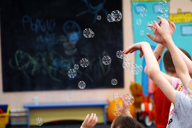 Kinder ziehen ihre Hände hinter Seifenblasen, die versuchen zu fangen