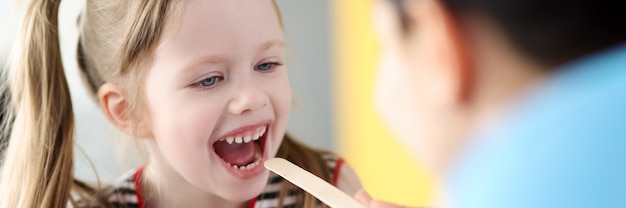 Kinderarzt, der den Hals eines kleinen Mädchens mit Spachtel untersucht