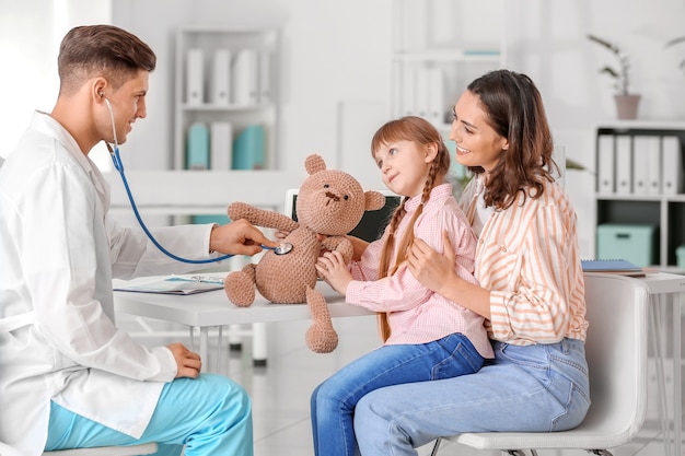 Kinderarzt mit Spielzeug, das kleinem Mädchen zeigt, wie man Stethoskop in der Klinik benutzt