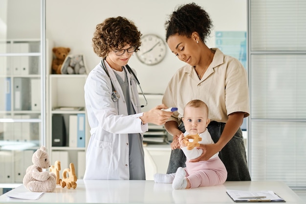 Kinderarzt untersucht das Baby mit spezieller medizinischer Ausrüstung während eines Krankenhausbesuchs mit seiner Mutter