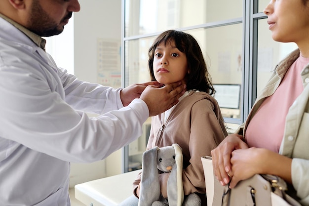 Kinderarzt untersucht die Halsschmerzen eines kleinen Mädchens, während sie mit ihrer Mutter zum Arzt geht