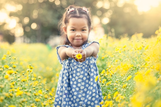 Kinderasiatisches kleines Mädchen, das Blume in ihrer Hand im Garten hält