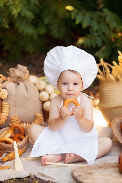 Kinderbäcker beim Picknick, das Brot und Bagels in der weißen Schürze und im Hut isst