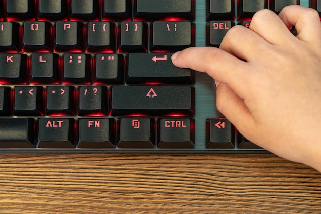 Kinderfinger drücken die Eingabetaste auf einer schwarzen Tastatur mit roter Hintergrundbeleuchtung