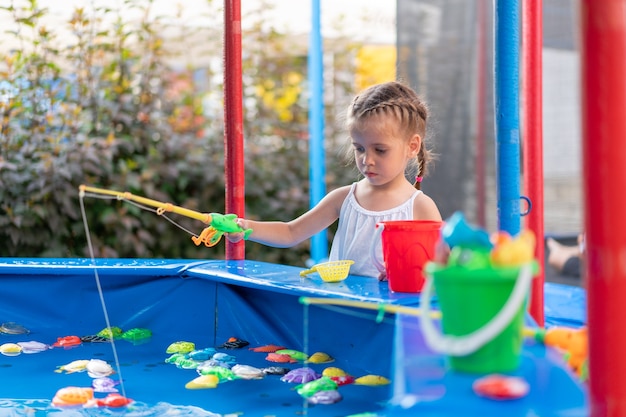 Kinderfischer fangen Plastikspielzeugfische am Pool Vergnügungspark Sommertag Kleines Mädchen haben Spaß beim Angeln Karneval Festival Unterhaltung für Kinder