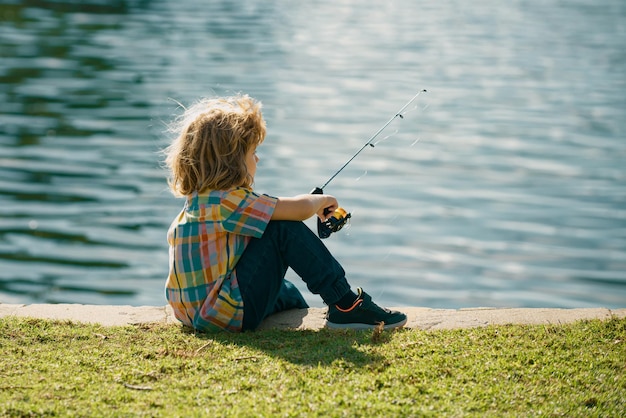 Kinderfischer Junge mit Spinner am Fluss Porträt eines aufgeregten Jungen beim Angeln Junge am Steg mit Angelrute Angelkonzept