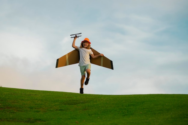 Kinderflieger mit Papierflügeln oder Spielzeugflugzeug träumt davon, im Sommer in der Natur zu reisen