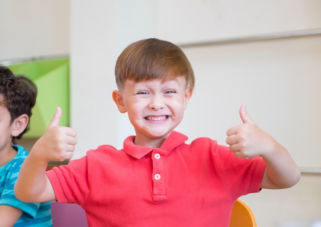 Kindergarten, criança, sorria e thumbs up classroom em pré-escola internacional, conceito de educação