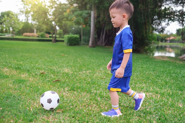 Kindergartenjunge in der Fußballuniform spielt Fußball