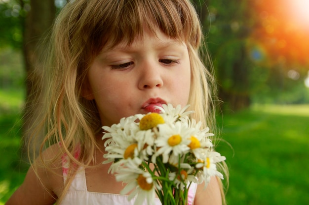 Kindergefühle, die zungenglückliches Mädchenkind mit einem Blumenstrauß im Naturpark zeigen